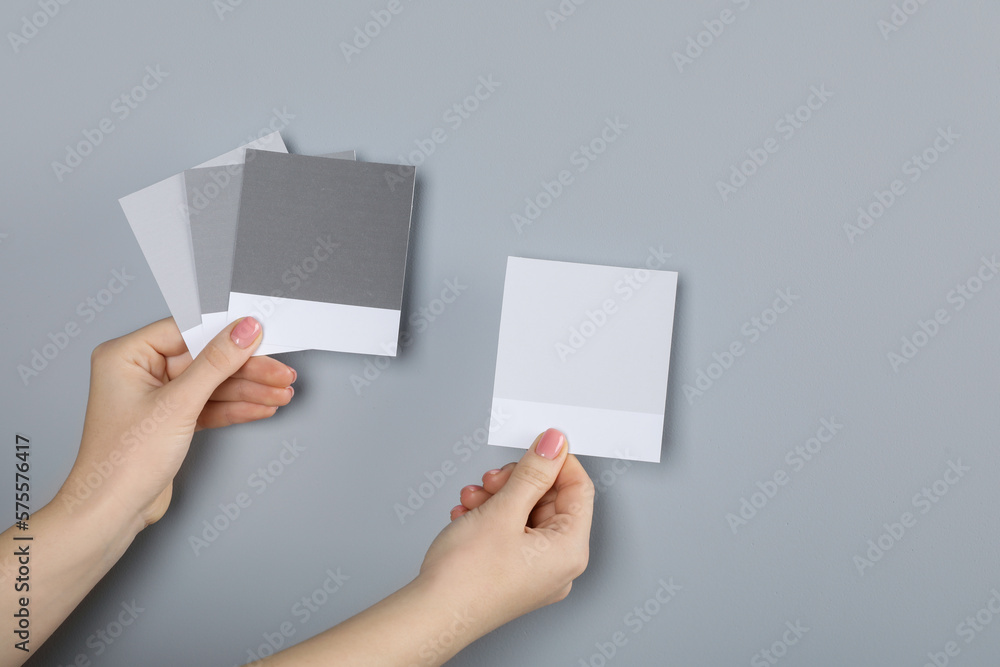 Woman with color sample cards choosing paint shade near grey wall, closeup. Interior design - obrazy, fototapety, plakaty 