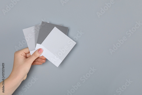 Woman with color sample cards choosing paint shade near grey wall, closeup. Interior design