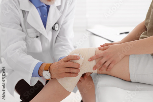 Foto Orthopedist applying bandage onto patient's knee in clinic, closeup