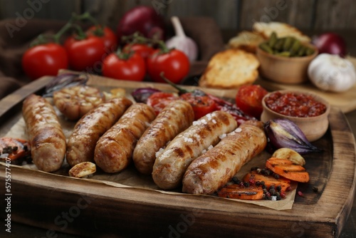 Tasty grilled sausages with vegetables on wooden table, closeup
