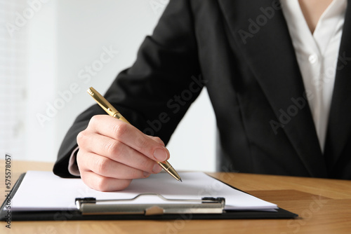 Woman with pen and clipboard at wooden table, closeup