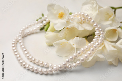 Beautiful pearl necklace and flowers on white marble table, closeup