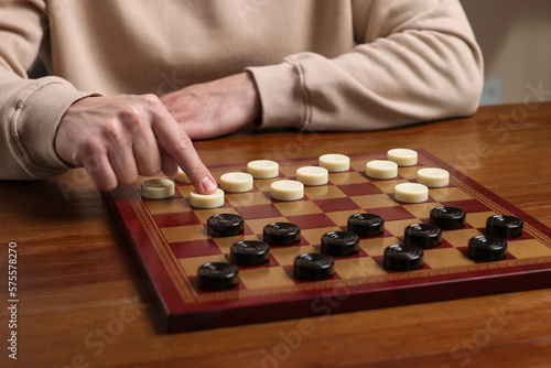 Playing checkers. Man thinking about next move at wooden table, closeup