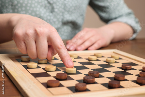 Playing checkers. Woman thinking about next move at wooden table, closeup