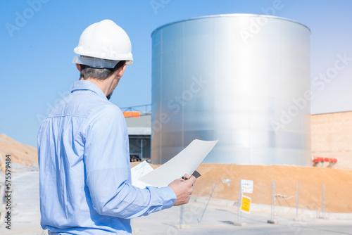 Civil engineer inspecting work with licenses and blueprints, standing outdoors at construction site