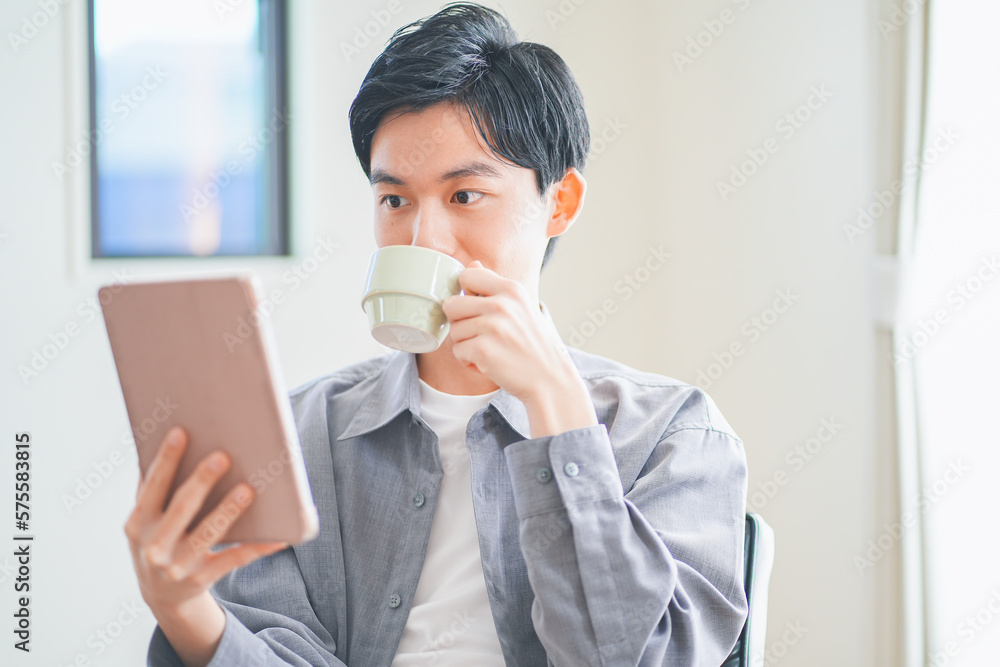 ソファでコーヒーを飲みながらタブレットを見る若い男性