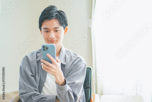 ソファに座ってスマートフォンを操作する若い男性