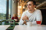 One man young adult Caucasian man sit at cafe or restaurant alone looking to the side having a cup of coffee real people copy space