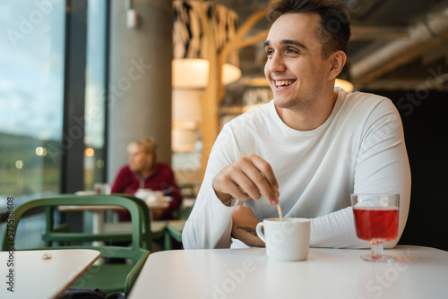 One man young adult Caucasian man sit at cafe or restaurant alone looking to the side having a cup of coffee real people copy space