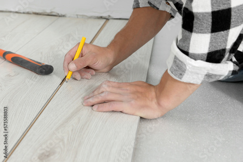 Professional worker using pencil during installation of new laminate flooring, closeup