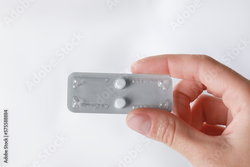 Woman holding blister of emergency contraception pills against blurred background, closeup