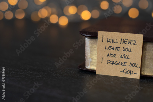 I will never leave you nor will I forsake you-God, handwritten verse on note and holy bible with golden pages with blurred golden bokeh background. Book of Hebrews 13:5 text.