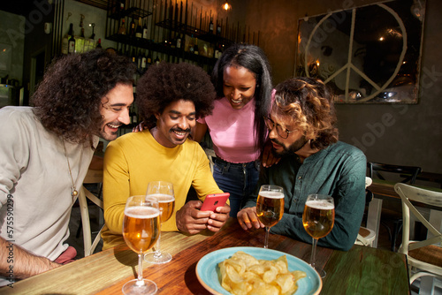 Canvas Print Group portrait multi-ethnic friends group watching smiling at cell phone at bar after work at pub happy hour