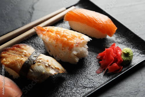 Serving board with delicious nigiri sushi, ginger and wasabi on black table, closeup
