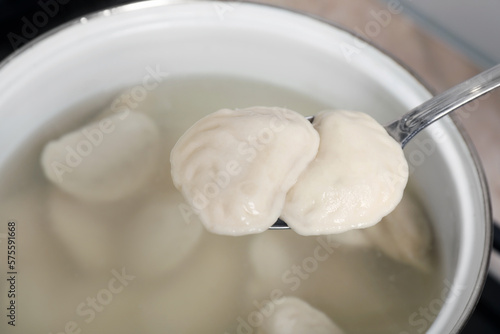Spoon with tasty dumplings (varenyky) over pot, closeup