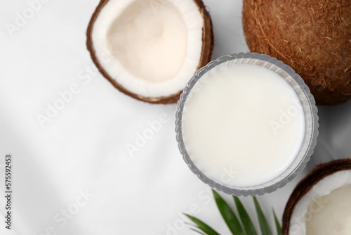 Glass of delicious coconut milk, palm leaf and coconuts on white table, flat lay. Space for text