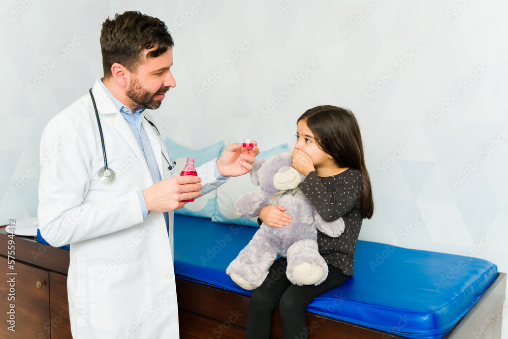 Fototapeta premium Scared girl refusing to take cough syrup medicine from the doctor