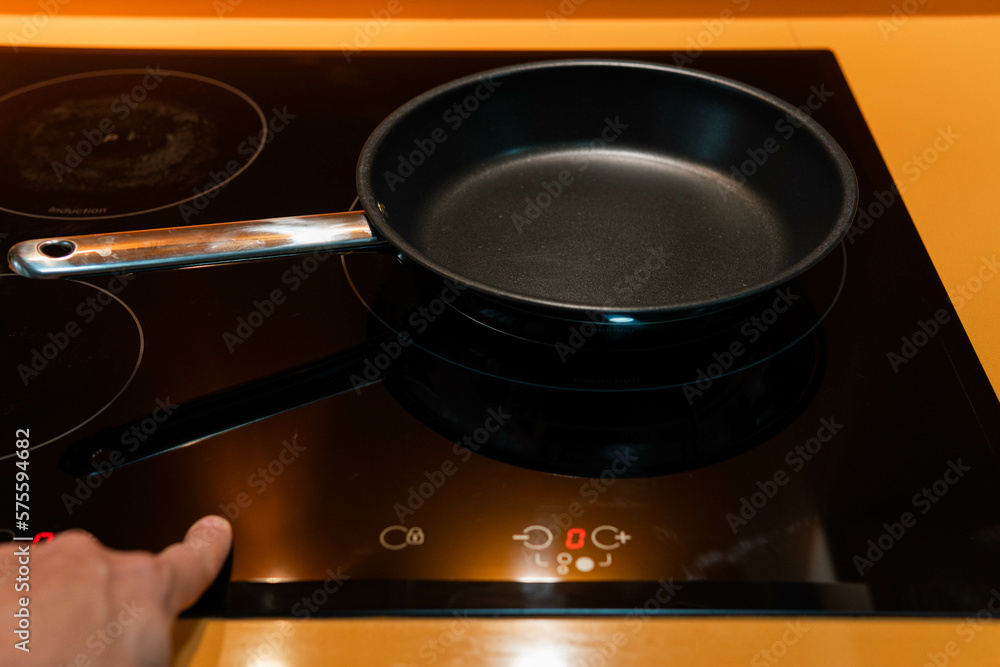 Close-up of frying pan with hand switching the induction in orange kitchen Close-up of frying pan with hand switching the induction in orange kitchen