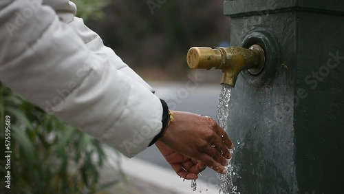 Wash your hands with water. Flowing water, outdoor public fountain.