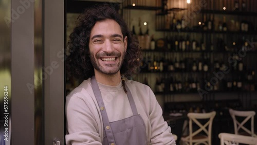 Close up video young adult local small business owner looking at camera. Happy male bartender with positive attitude. Cheerful worker smiles while standing leaning on bar door. Confident people. 