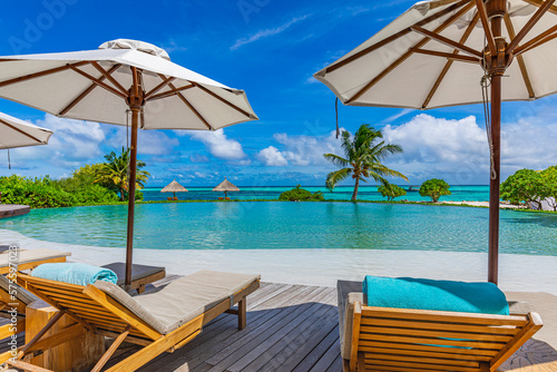 Outdoor tourism landscape. Luxurious beach resort with swimming pool and beach chairs or loungers under umbrellas with palm trees and blue sky. Summer travel and vacation background concept 