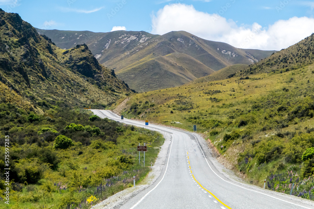Winding and scenic road in New Zealand, with mountains and blue sky Winding and scenic road in New Zealand, with mountains and blue sky