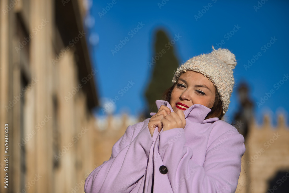 Portrait of a young woman, beautiful, straight brown hair, sweater, coat and wool hat, covering her face with her coat to protect herself from the cold. Concept beauty, fashion, autumn, winter, cold.