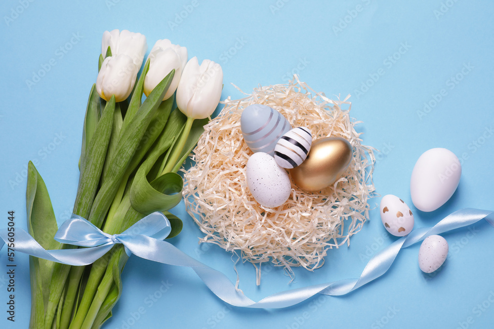 Fototapeta premium Many painted Easter eggs, tulip flowers and ribbon on light blue background, flat lay