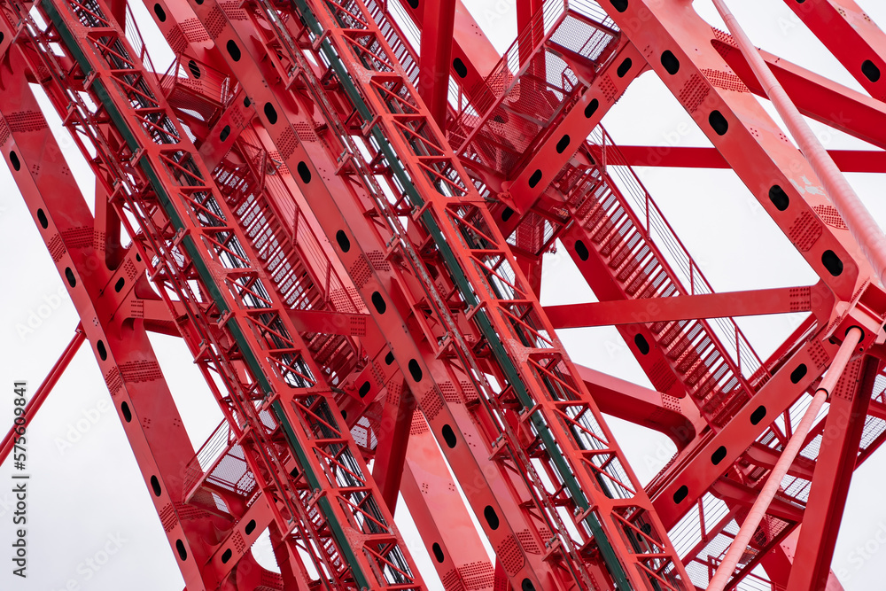 Close-up of fragment of red cable-stayed bridge pylon in place where metal cables are fastened. Close-up shows connection of steel powerful straight crossbar, bridge connection, metal architecture. Close-up of fragment of red cable-stayed bridge pylon in place where metal cables are fastened. Close-up shows connection of steel powerful straight crossbar, bridge connection, metal architecture.