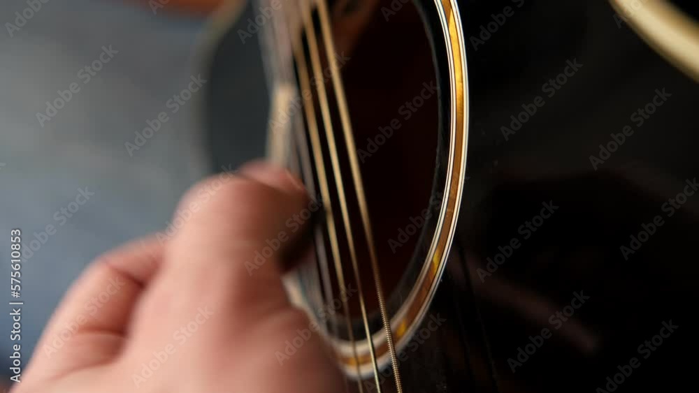 Playing the guitar. Strumming black acoustic guitar. Musician plays music. Man fingers holding mediator. Male hand playing guitar neck in dark room. Unrecognizable person rehearsing, fretboard closeup Playing the guitar. Strumming black acoustic guitar. Musician plays music. Man fingers holding mediator. Male hand playing guitar neck in dark room. Unrecognizable person rehearsing, fretboard closeup
