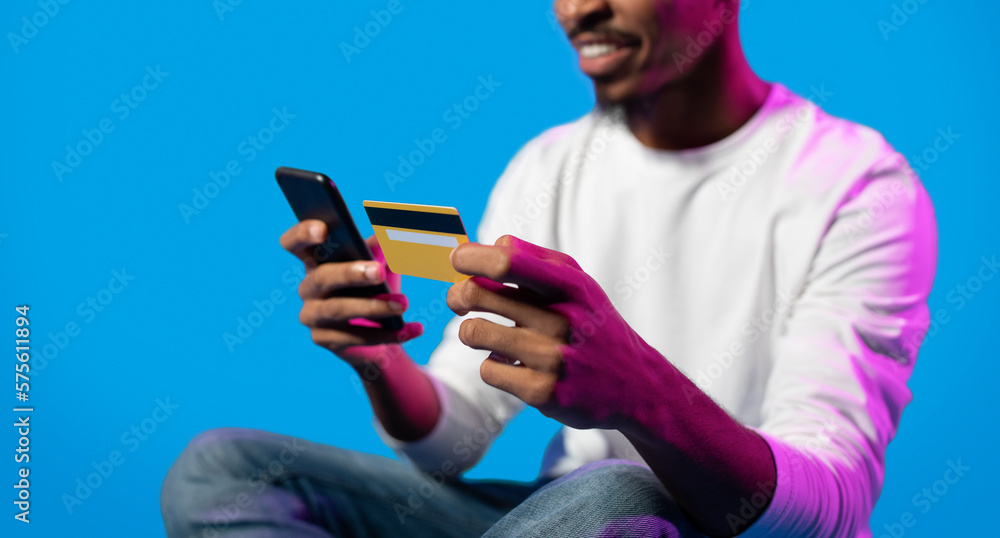Fototapeta premium Unrecognizable black guy holding smartphone and credit card, cropped