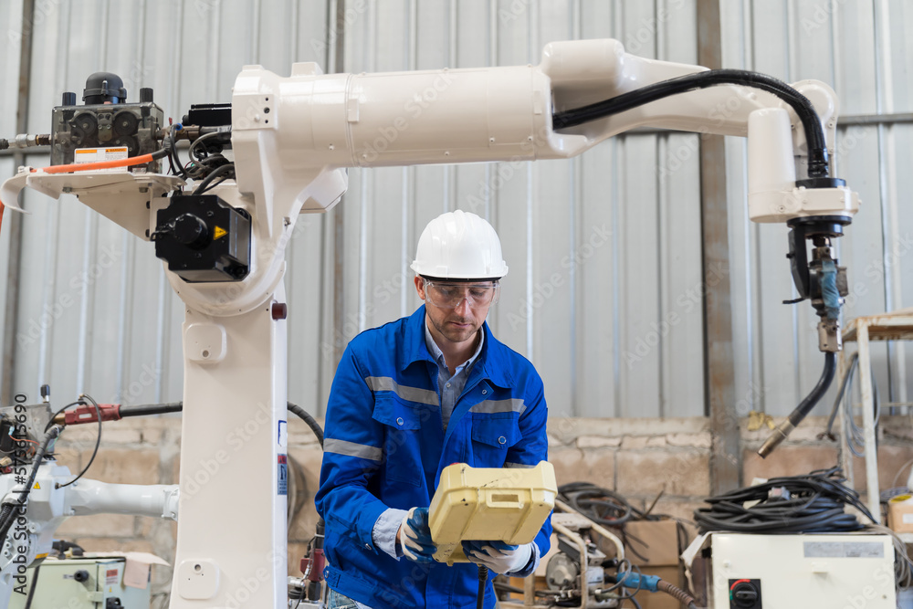 Male engineer worker wear safety uniform, helmet and gloves control robot arm welding at production line plant factory Male engineer worker wear safety uniform, helmet and gloves control robot arm welding at production line plant factory