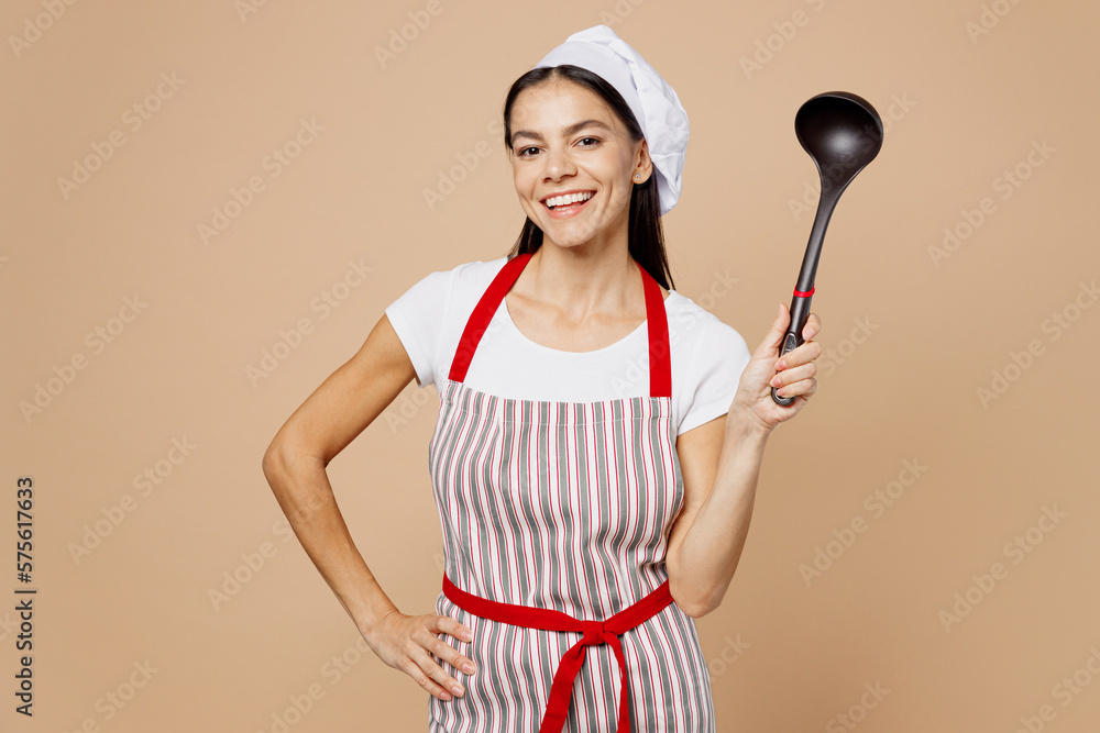 Young smiling happy cheerful fun housewife housekeeper chef baker latin woman wears striped apron toque hat hold laddle look camera isolated on plain pastel light beige background Cook food concept Young smiling happy cheerful fun housewife housekeeper chef baker latin woman wears striped apron toque hat hold laddle look camera isolated on plain pastel light beige background Cook food concept