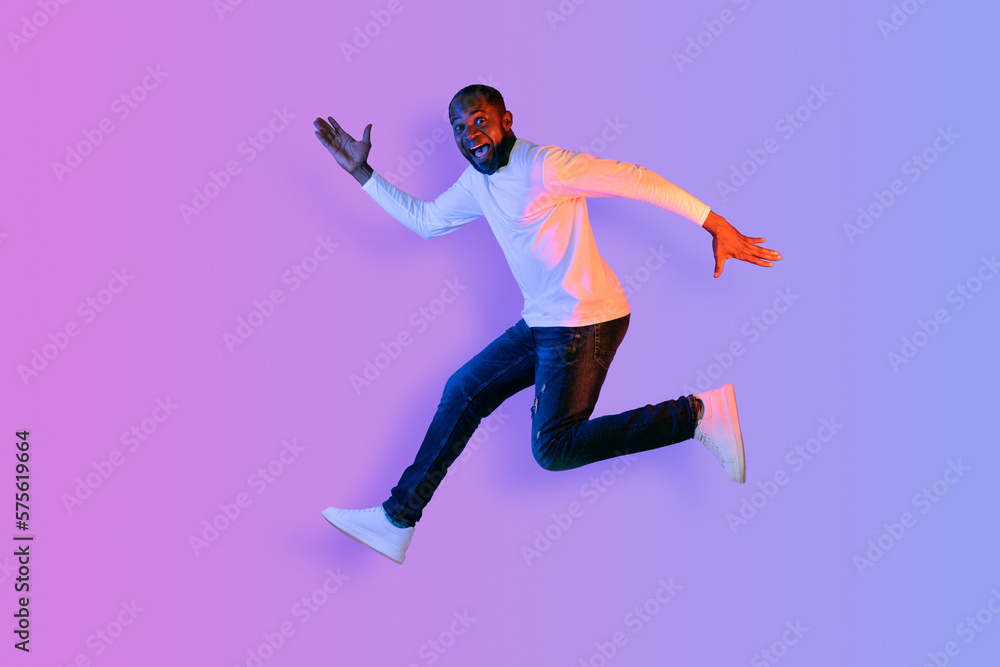 Emotional african american man running over neon studio background Emotional african american man running over neon studio background