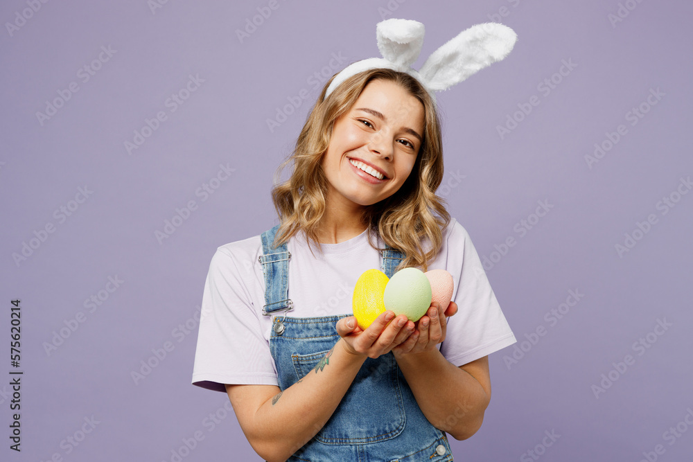 Young surprised cheerful woman wear casual clothes bunny rabbit ears hold in hands palms colorful eggs isolated on plain pastel light purple background studio portrait. Lifestyle Happy Easter concept. Young surprised cheerful woman wear casual clothes bunny rabbit ears hold in hands palms colorful eggs isolated on plain pastel light purple background studio portrait. Lifestyle Happy Easter concept.