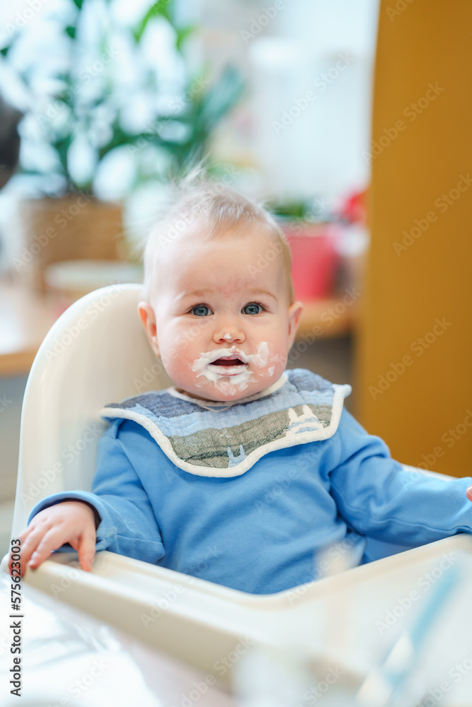 Funny portrait of a baby toddler with a dirty face sitting in the kitchen in a high chair Funny portrait of a baby toddler with a dirty face sitting in the kitchen in a high chair