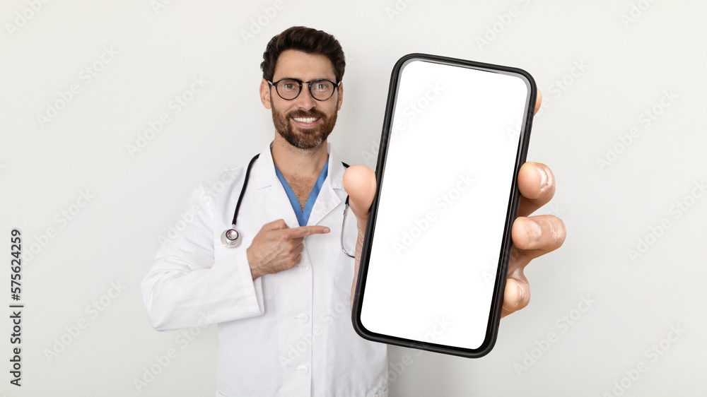 Telemedicine Concept. Handsome male doctor pointing at blank smartphone in his hand