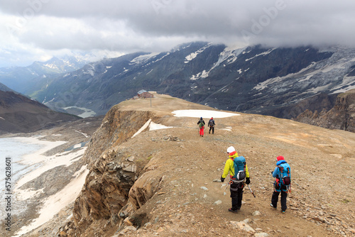 Group of people hiking towards alpine hut Oberwalderhütte and mountain snow panorama in Glockner Group, Austria