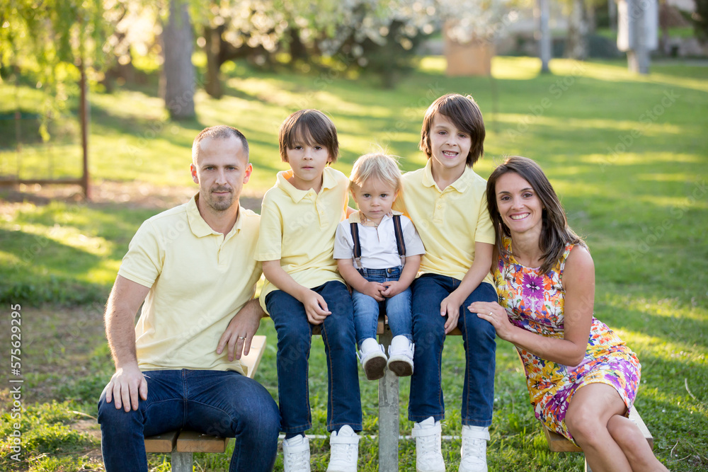 Fototapeta premium Beautiful family, mother, father and three kids, boys, having familly outdoors portrait taken on a sunny spring evening, beautiful blooming garden, sunset time