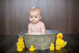 Cute baby playing with rubber duck while sitting in metal basin