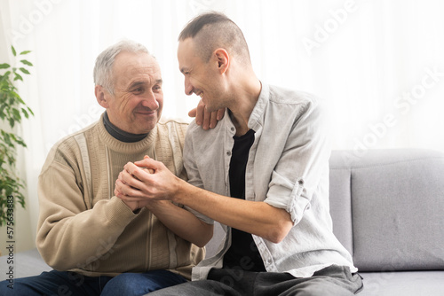 Young adult caucasian son listening and supporting his old elderly senior father at home indoors. Care and love concept.