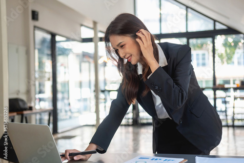 Asian businesswoman in a black suit working in an office using a laptop and profit calculator for business, concept business