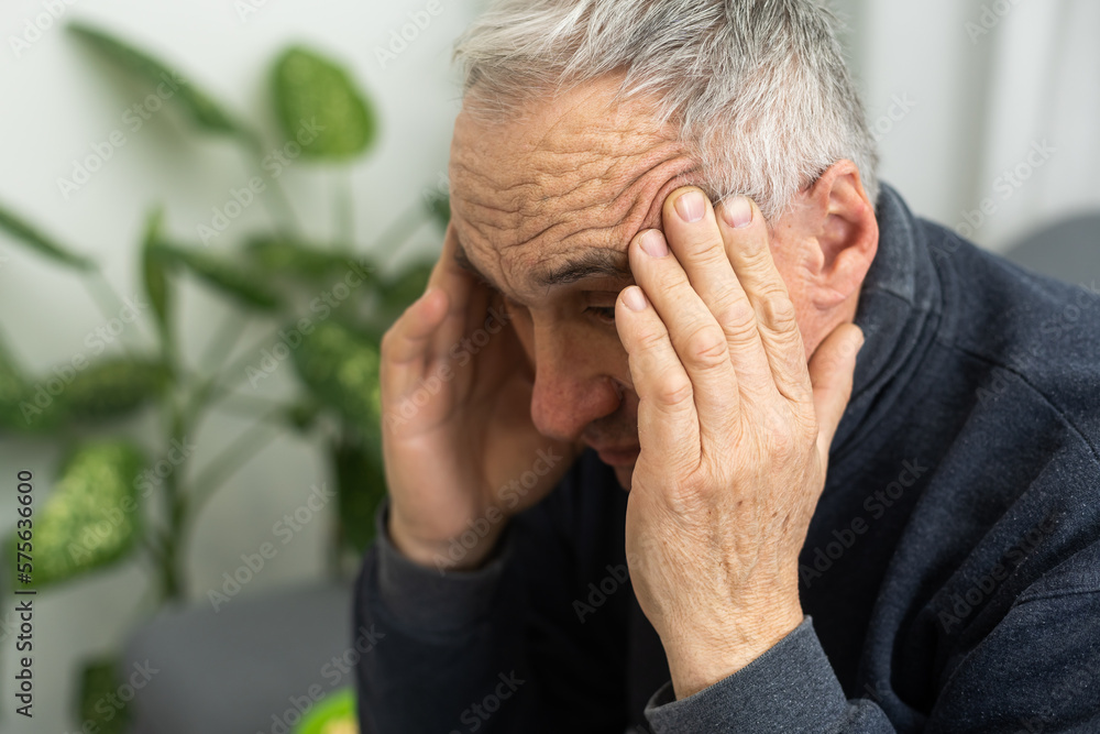 Fototapeta premium Tired old man suffering from headache, massaging his temples. Strong migraine attack. An elderly man has a headache, massaging his temples