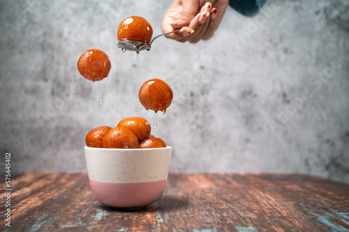 A girl serving Gulab Jamun in a bowl with pouring sweet syrup. photo