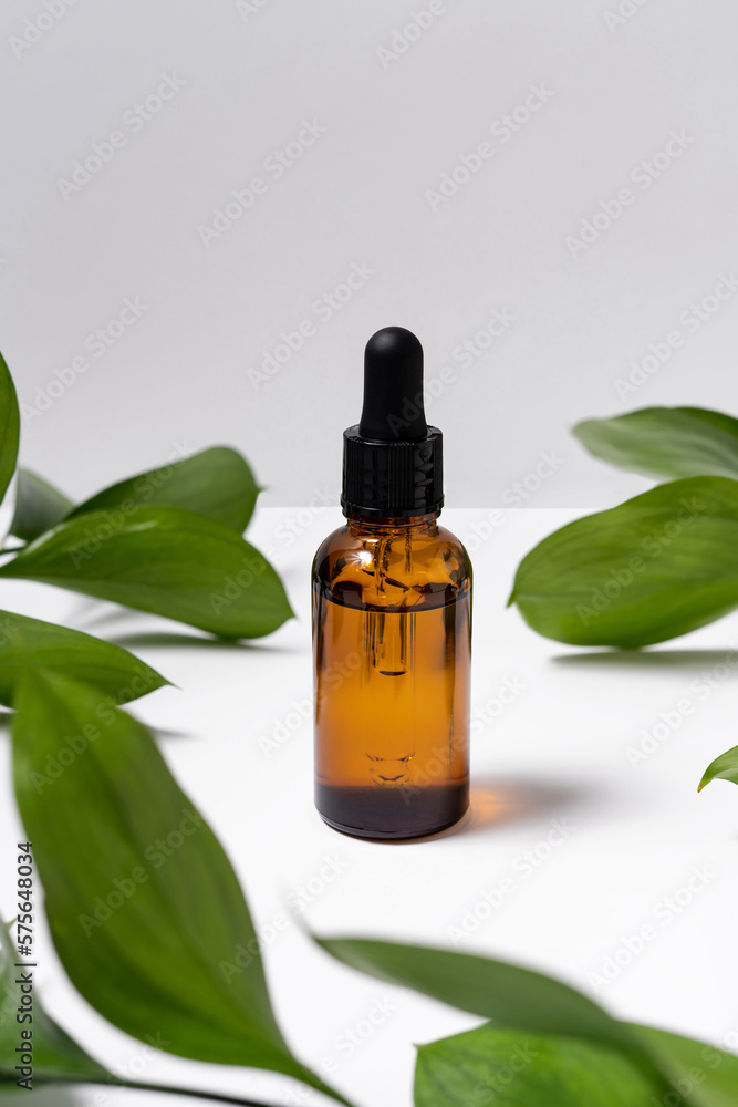 Glass brown reusable bottle for natural serum on white isolated background with green plant leaves. Cosmetic product presentation or image for your design Glass brown reusable bottle for natural serum on white isolated background with green plant leaves. Cosmetic product presentation or image for your design
