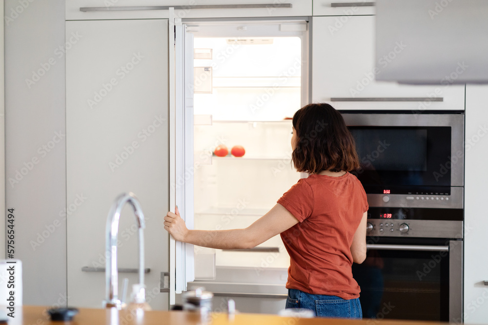 Young Housewife Searching For Food In Empty Fridge In Kitchen Young Housewife Searching For Food In Empty Fridge In Kitchen