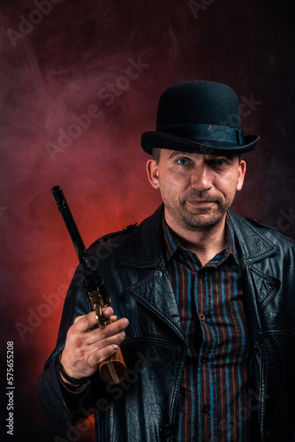 Dangerous gangster. Bandit with a weapon. A man in a casual coat, shirt and hat with a gun. An old man with stubble and a bad temper.