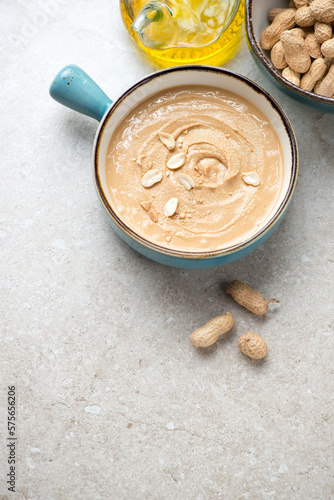 Peanut butter in a turquoise serving bowl on a beige stone background, vertical shot, copy space, elevated view