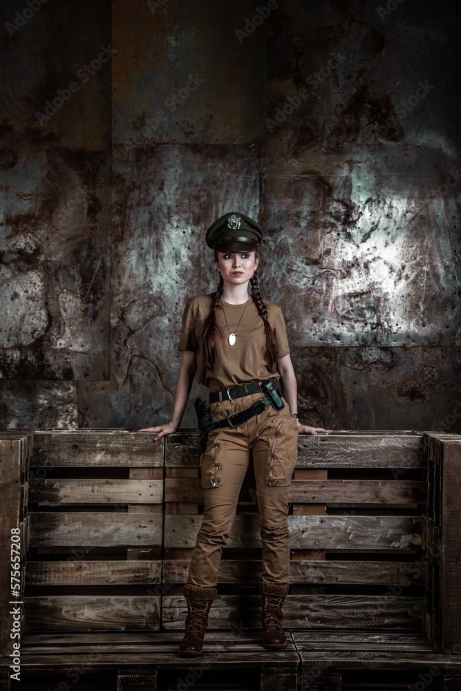 American pilot. A beautiful young woman in a uniform and with a weapon on the background of a metal wall. Staged photo. Studio light.