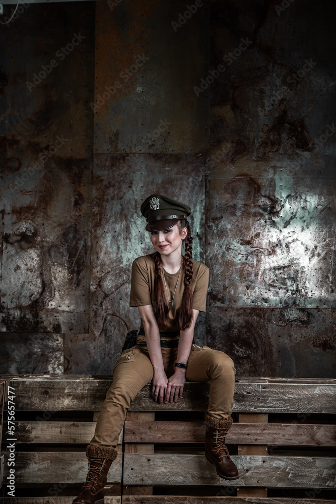 American pilot. A beautiful young woman in a uniform and with a weapon on the background of a metal wall. Staged photo. Studio light.